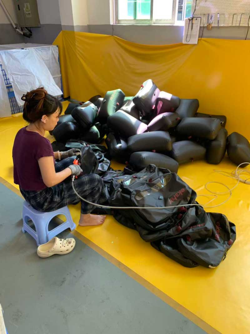 Operator inflating welded travel bags through their air valves beside a pile of inflated units