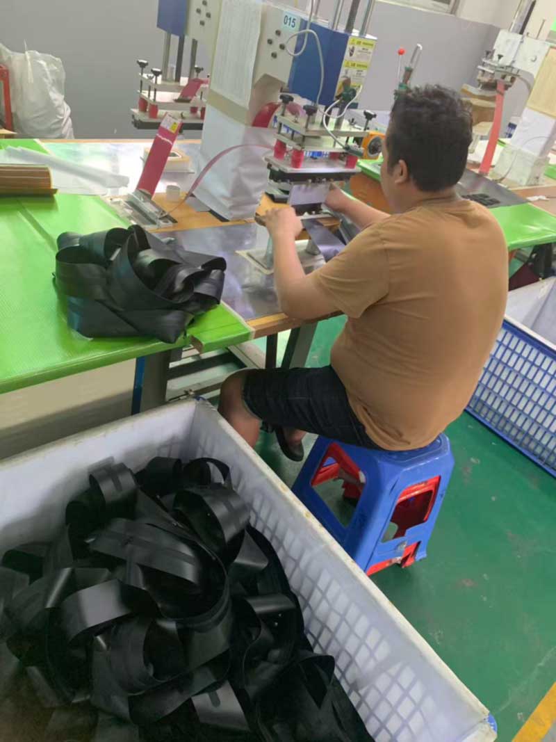 Welded webbing loops and anchor components accumulating in a lined bin at a welding station