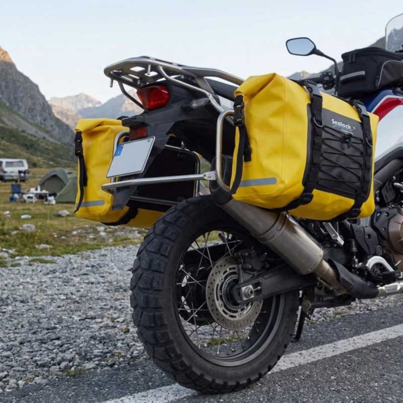 Twin waterproof panniers mounted on a touring motorcycle showing exhaust and wheel clearance